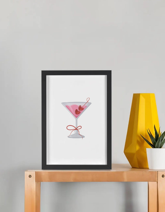 Framed poster with pink cocktail design – black frame on wooden shelf, minimal wall art for modern decor